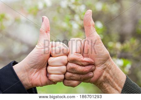 Close up picture of a senior and a young female's hand showing thumbs up outdoor