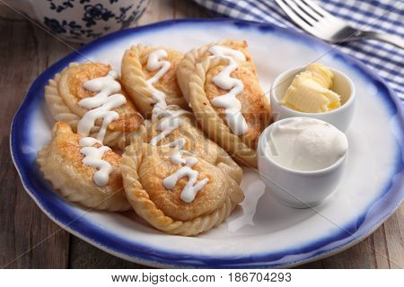 Traditional Polish dumplings Pierogi ruskie with sour cream and butter on a rustic table
