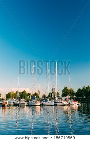 Riga, Latvia. Many Yachts Moored At The City Pier Harbour Bay And Quay In Summer Sunny Evening. Reflections From Boats In The lear Water Of Western Dvina River.