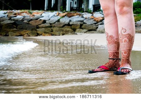 Girl's feet with henna tattoos and sandles. She is standing on a sandy beach probably on a honeymoon vacation