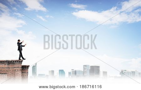 Businessman with blindfolder on eyes walking on building top