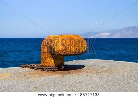 Rusty bitt with a chain on the berth. In the background of sea and mountains.