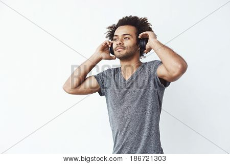 Young handsome african man listening to music in headphones over white background. Copy space.
