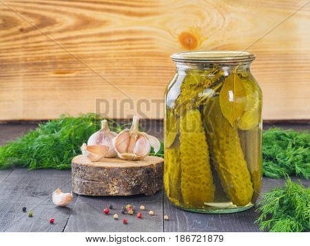 Pickled cucumbers on wooden background. Pickles in glass jar with garlic, peppercorn and fresh dill. Salted cucumber in jar with copy space