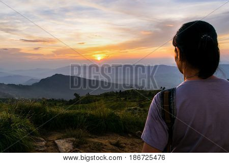 Woman tourist looking beautiful nature of colorful sky during the sunset over the mountain at view point Phu Chi Fa Forest Park in Chiang Rai Province Thailand