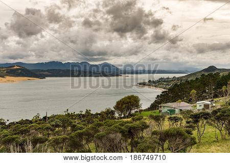 Bay of Islands New Zealand - March 7 2017: Opononi town on shore of Hokianga Harbour seen from Ti Pikinga Reserve. Wide shot of mountains the Hokianga River bush country all under heavy cloudscape