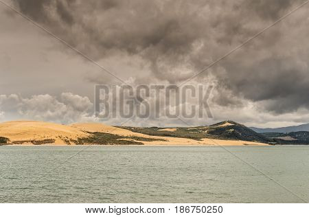 Bay of Islands New Zealand - March 7 2017: Exit to Tasman Sea from Hokianga Harbour shows large dune under heavy cloudscape because of approaching cyclone.