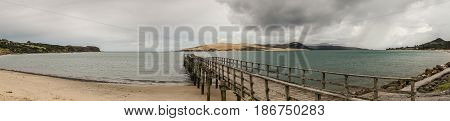 Bay of Islands New Zealand - March 7 2017: Panorama shot of exit to Tasman Sea from Hokianga Harbour shows large dune pier mountains all under heavy cloudscape because of approaching cyclone.