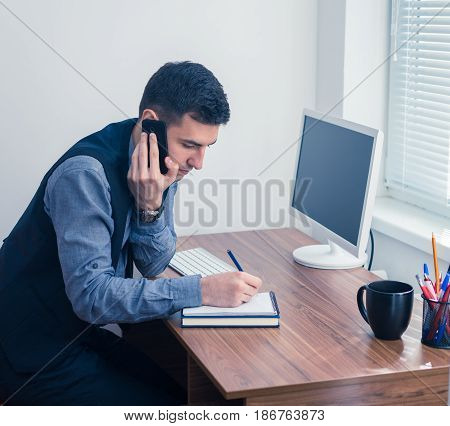 An office worker works at a computer in the office and takes an order by phone. Office concept with working environment.