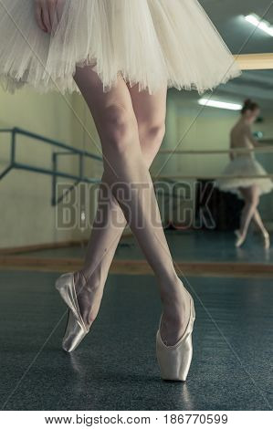 Ballerina in pointe shoes and tutu warming up before dance lessons. Crossed long slender female feet. Classical ballet. Prima ballerina.