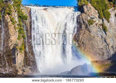 Magnificent rainbow in the spray of the waterfall Montmorency in Montmorency Falls Park.  Above the waterfall built bridge for walking. The concept of active and cultural tourism