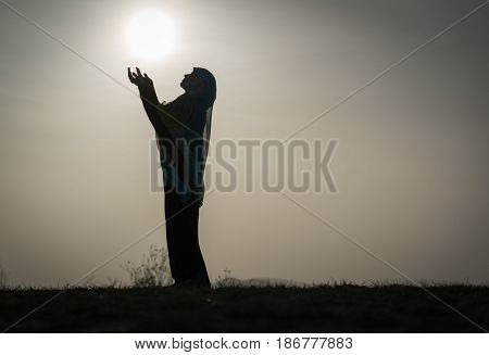 Silhouette Muslim Arabic woman praying with her hands up