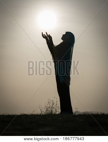 Silhouette Muslim Arabic woman praying with her hands up