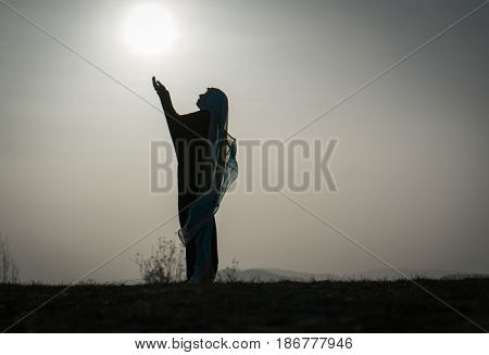 Silhouette Muslim Arabic woman praying with her hands up