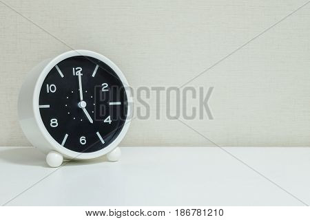 Closeup black and white alarm clock for decorate in 5 o'clock on white wood desk and cream wallpaper textured background with copy space
