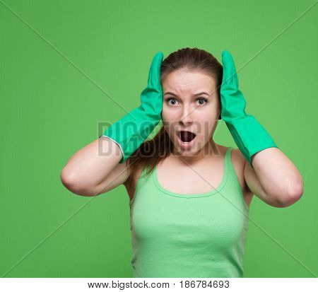 Tired frustrated and shocked cleaning woman screaming. Stressed spring cleaning woman in green rubber gloves looking at camera. Isolated on green background