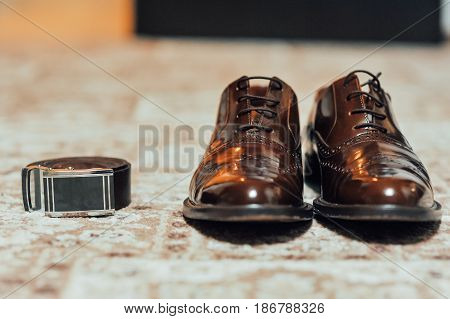 A new pair of tan leather shoes and belt on beige carpet
