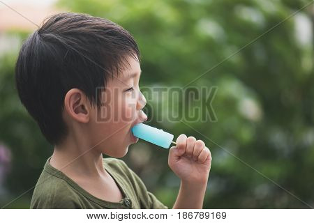 Cute Asian child eating blue ice cream outdoors