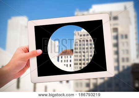 Masculine hand holding tablet against building structures against blue clear sky