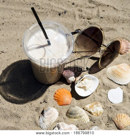 Ice latte on sand with cockleshells and glasses