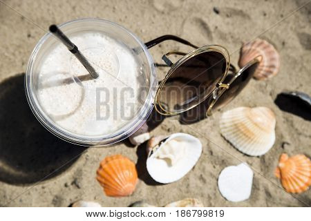 Ice latte on sand with cockleshells and glasses