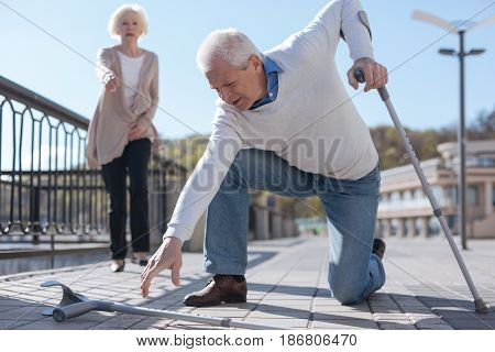 Difficulties of retirement. Gentle baffled panicky man leaning on one crutch raising another one from the ground while polite woman expressing readiness for help