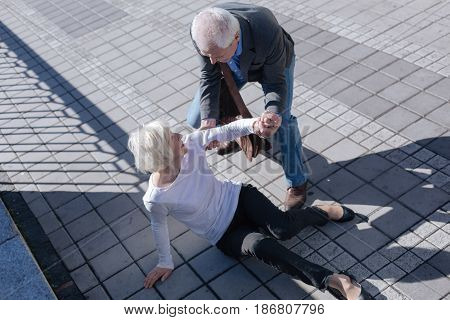 Do not afraid of falling down. Funny white-haired slim lady catching foot and receipting of relief from aged man who smiling