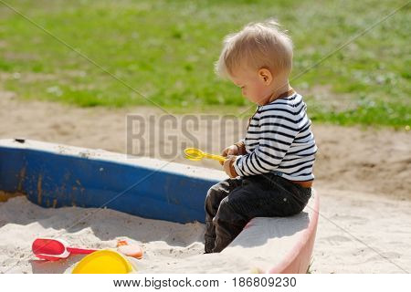 Portrait of toddler child outdoors. One year old baby boy playing with sand at playground sandbox