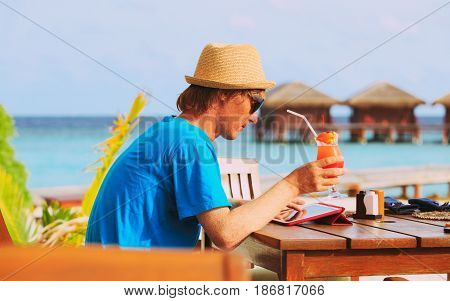 youg man drinking cocktail looking at touch pad on tropical beach resort
