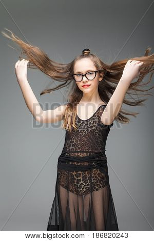 young girl in stylish glasses throws up his long curly hair. She is dressed in a black dance dress with a leopard pattern