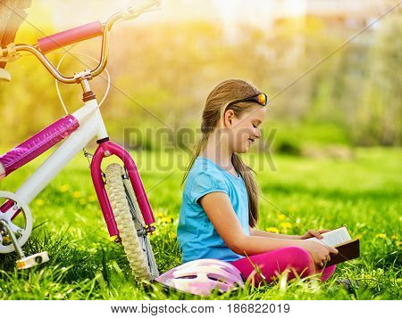 Bikes cycling kid girl. Child girl rides bicycle. Girl in cycling reading book near bicycle into park outdoor. Cyclist looking at book. Schoolgirl does homework in nature.