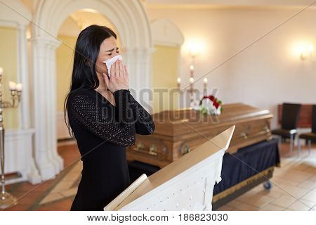 burial, people, grief and mourning concept - close up of sad woman with napkin crying near coffin at funeral in church