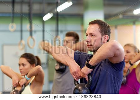 sport, fitness, weightlifting and training concept - group of people with kettlebells and heart-rate trackers exercising in gym
