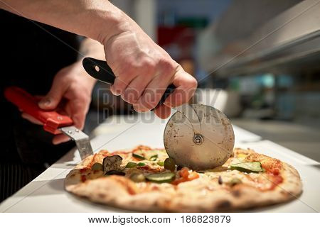food, italian kitchen and cooking concept - cook with cutter cutting pizza to pieces at pizzeria