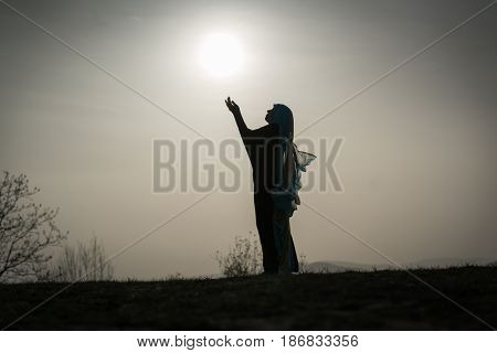 Silhouette Muslim Arabic woman praying with her hands up