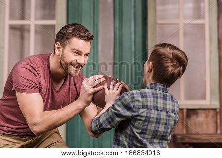 Father With Little Son Playing American Football With Ball At Backyard, Dad And Son Playing
