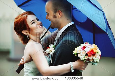 Happy Bride Hugs A Groom Under Blye Umbrella