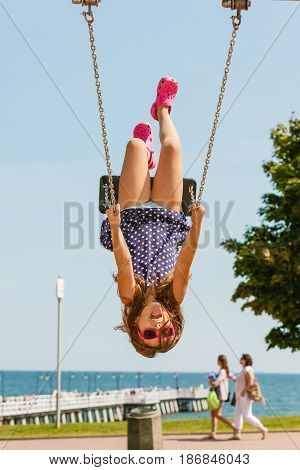 Craziness and freedom. Young summer girl playing on swing-set outdoor. Crazy playful child swinging very high to touch the sky.