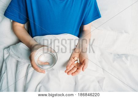 Partial View Of Boy Holding Glass Of Water And Medicines In Hospital Bed, Hospital Patient Care Conc