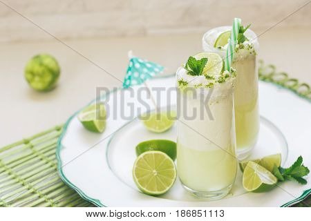 Refreshing  Brazilian lemonade or limeade in two sugar rimmed glasses,  decorated with lime slices and mint . Macro, selective focus, blank space