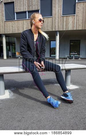 Full length of sporty young woman in sportswear listening music while sitting on bench