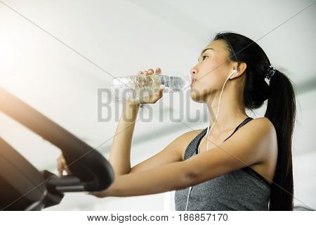 Asian woman in sportswear drinking water after workout at the gym.