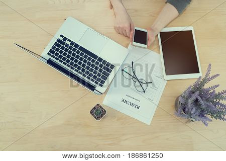 woman hold and touch blank screen on cell phone smartphone with Resume information modern glasseslaptop tablet and Cactus flower on pot. Concept of jop search.
