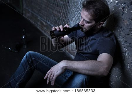 Suffering from my loneliness. Mature bearded addicted freak sitting on the floor in the darkness while being stoned and drinking alcohol