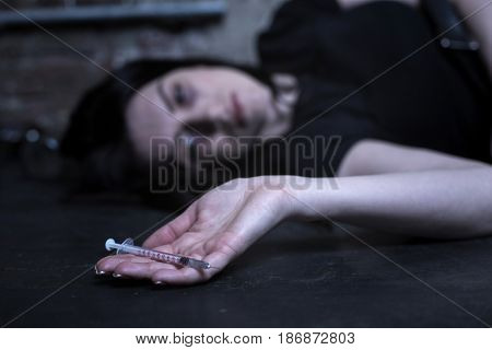 Waiting for my death. Obsessed homeless tired woman lying in the dark place and holding empty syringe while expressing apathy