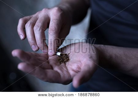 Illegal way of relaxation. Neglected young marijuana addicted man holding marijuana cigarette while getting new drug and waiting for dose