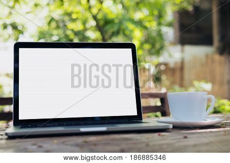 Mockup image of laptop with blank white screen and coffee cup on vintage wooden table in nature outdoor park