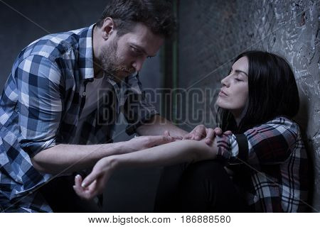 Sharing illegal depressant. Skilled fearless stoned freaks sitting on the ground while sharing new dose and injecting drug