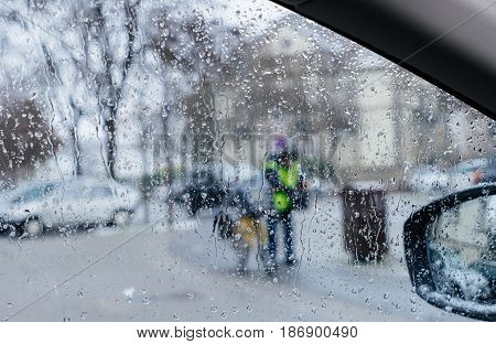 Silhouette of postman postal worker on bike crossing street on a snowy day - senn by the driver point ov view personal perspective through wet windshield window