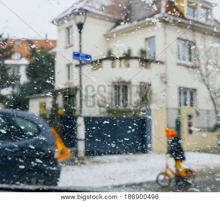 Silhouette of child kid on bike crossing street on a snowy day - senn by the driver point ov view personal perspective through wet windshield window
